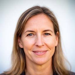 Portrait von Gerta Hinck vor einer hellen Wand mit selbstbewusstem, freundlichem Ausdruck